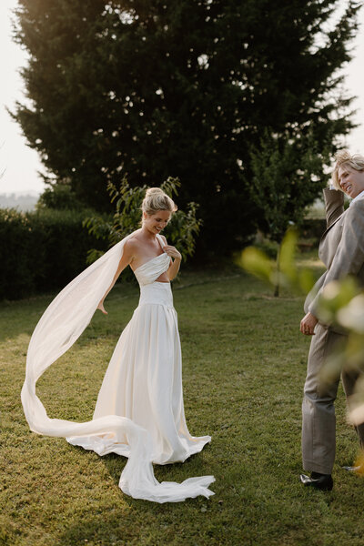 A person in a wedding dress adjusting their veil as their partner looks on 