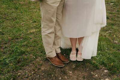 A bride and a groom standing next to each other showing off their shoes in Colorado. 