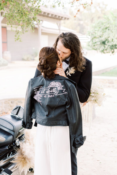 bride and groom kissing in leather jacket next to motorcycle at Giracci Vineyards