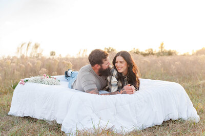 Couple looking at each other in admiration while laying in a field at sunset