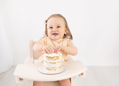 1 year old girl in high chair with cake smash