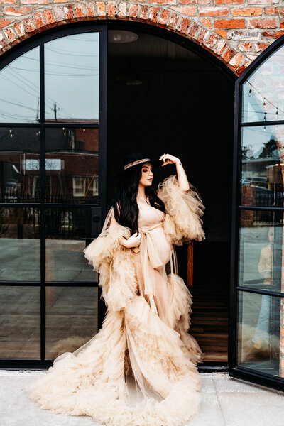 a beautiful pregnant mama in front of a venue door holding her belly in a gorgeous tan robe