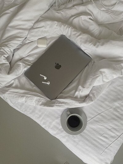 Laptop on bed with a coffee and airpods