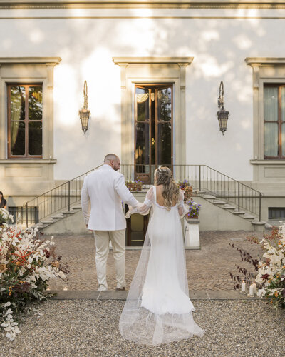 A couple walks hand-in-hand toward a grand venue entrance, coordinated by WINK! Weddings for a luxurious Colorado wedding celebration.