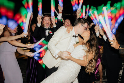 Different Pointe of View Wedding Photographer and Videographer Couple Dip Kissing with Guests Holding Glowsticks