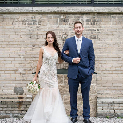serious bride and groom in front of brick wall