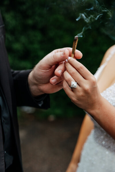 bride and groom hands with beautiful diamond ring holding a smoking joint after their wedding