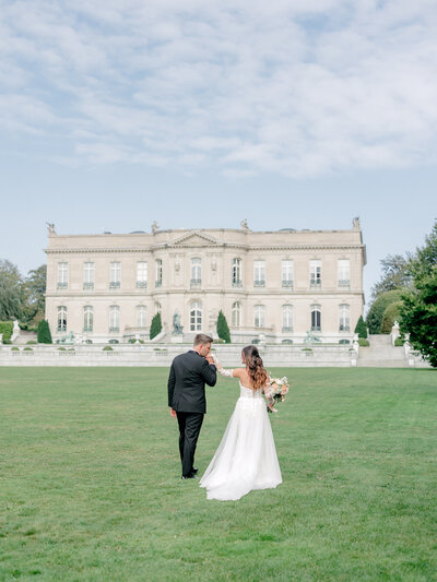 Groom kisses bride's hand in front of the The Elms in Newport, Rhode Island