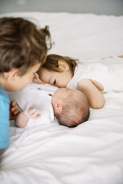 big siblings snuggling with newborn baby