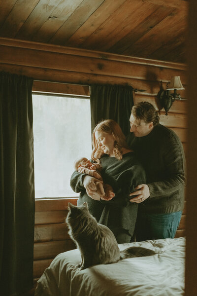 newborn lifestyle photo of a mom and dad holding baby  in a cabin with a cat