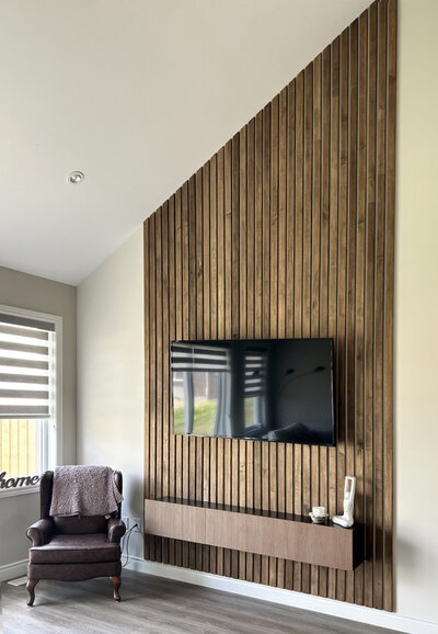 A vertical wooden slats accent wall with a TV and floating shelf hanging on it
