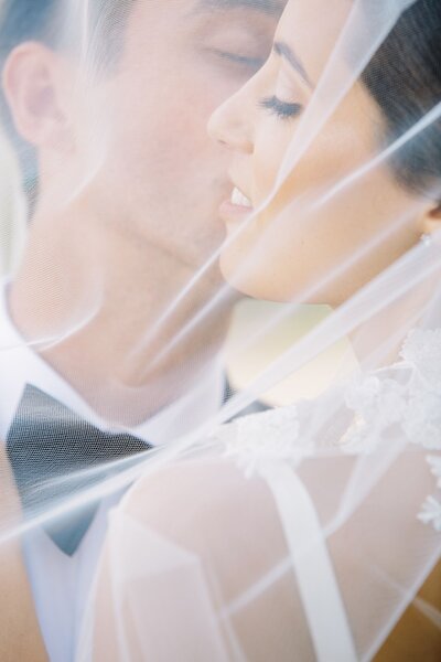 Bride and groom kissing under veil