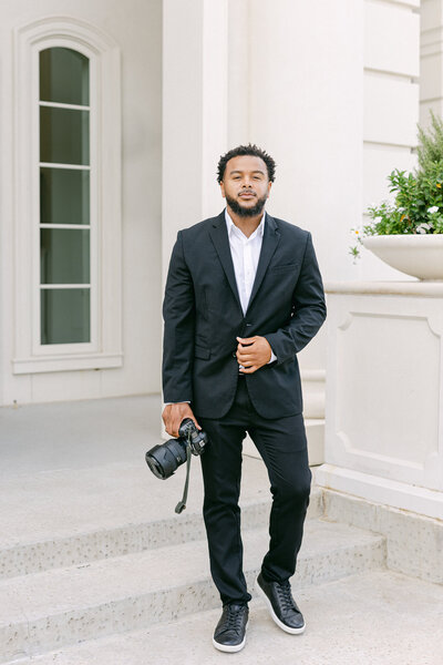 Larry in a black suit holding a camera