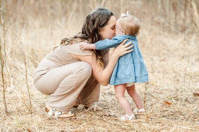 A young mother bends down and gives her toddler daughter kisses during a family session near the Outer Banks.