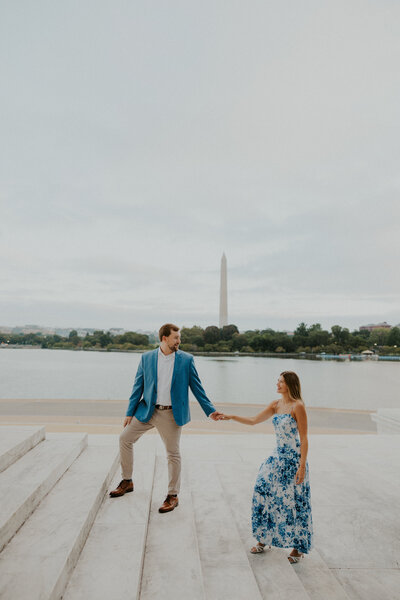 Engaged couple standing on the steps of the Thomas Jefferson Memorial with the Tidal Basin and Washington Monument in the foreground.