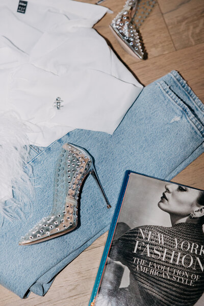 Flash photo of a white top, jeans, sparkly heels, and a fashion book on a wood background