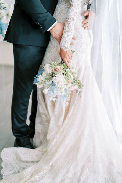 Bride holding pastel bouquet with groom, detail shot of lace gown captured near Toronto