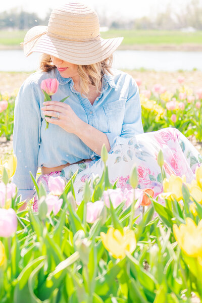 woman smelling flower sitting in tulip field