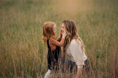 Little girl standing in a field in Ottawa, touching her moms cheeks.