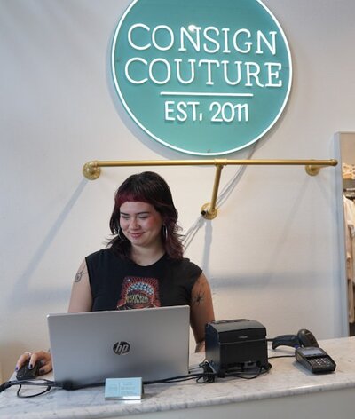 A person behind a register working on a laptop 