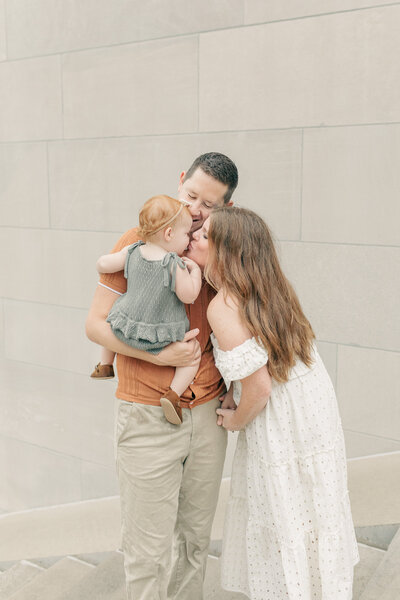 A loving family moment with a mother, father, and toddler embracing on a stone staircase in Kansas City. 