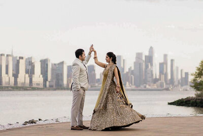 Bride and groom walk along waterfront with New York City skyline in background – NYC wedding photo by Alex Kaplan