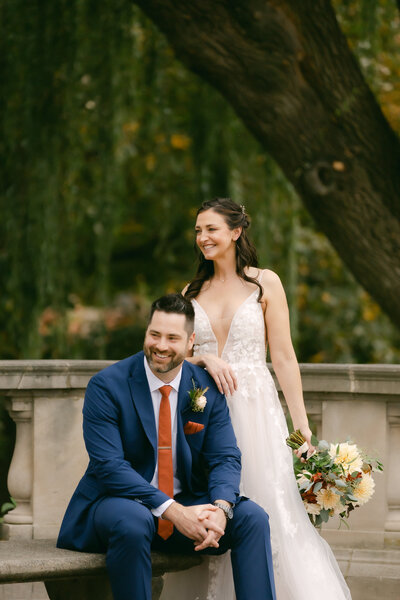 A couple stands in front greenery in New York City after getting married.