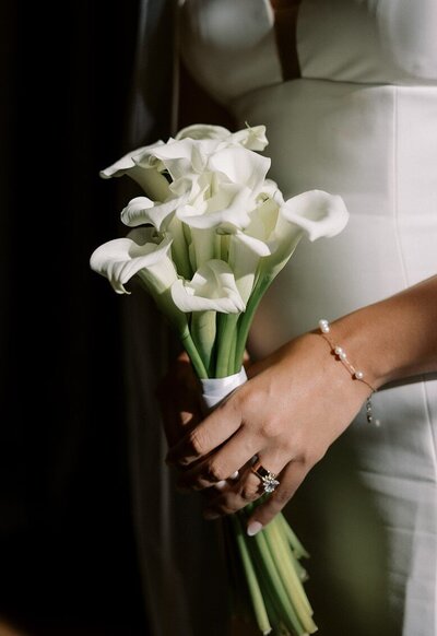 Close-up of a bride holding white calla lilies, showcasing bouquet and jewelry, photographed in a candid, documentary style by Chicago wedding photographer Abe Fernandez