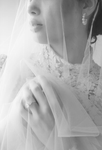 Black and white close-up photo of a bride's ring and her veil over her face