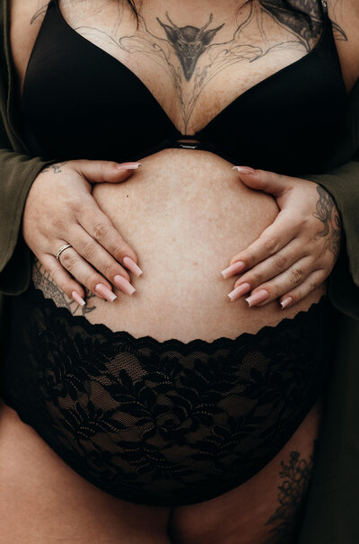 En närbild på en gravid kvinnas gravidmage med hennes händer på magen under en gravidfotografering i Stockholm