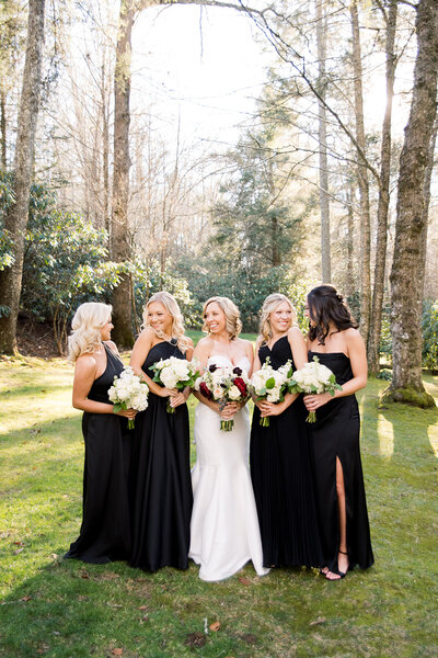 woman in the middle wearing white dress holding flowers standing next to girls in black dresses holding flowers