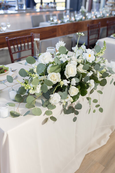 Elegant wedding reception centerpiece with white and blush roses, designed by Leigh Florist, surrounded by candlelight in a romantic venue setting.