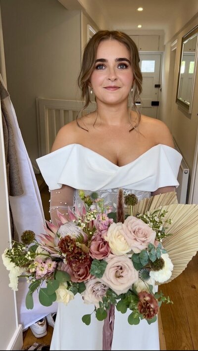 Bride and Groom exchanging vows under outdoor wedding pergola at Eden Barn Cumbria Lake District with flower arch flower installation apricot flowers pampas eucalyptus