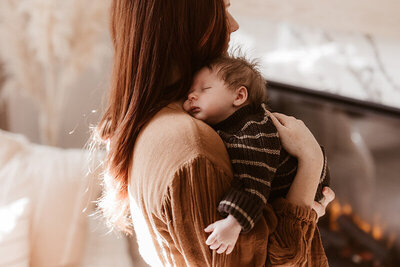 Mom holding newborn baby boy over her shoulder while wearing a knit brown and tan stripped sweater