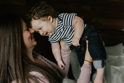 A mother lifts her baby boy in the air while laughing