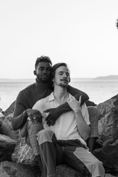 Queer gay couple sitting embracing on the coves in Seattle with the ocean in the background