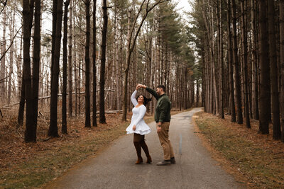 Couple captured in the woods during fall, with bare trees creating a serene, intimate atmosphere, showcasing their love in a quiet setting.