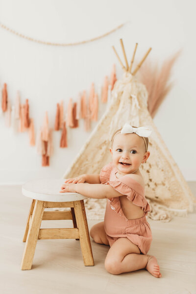 toddler girl in a white studio sitting in front of a lace teepee