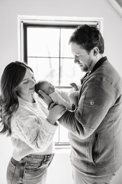 A couple holding their newborn baby in natural light within their home in black and white.