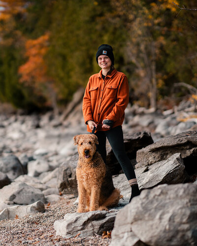 Alex, a wedding photographer, smiling outdoors in New York with her Airedale Terrier, Weller.