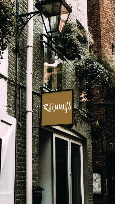 A photo stylized to look romantically vintage with a Vinny's restaurant sign created by Ayanna Richilano Designs attached to a pipe going up the brick wall