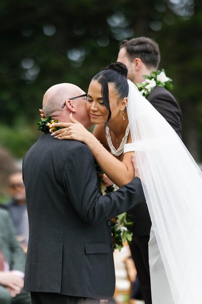 A person in a wedding dress leaning down as a loved one kisses their cheek 