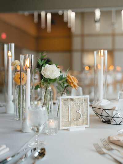 Rattan table number sitting on a wedding tablesetting amongst candles and flowers representing full service design and calligraphy by Life in Letters.