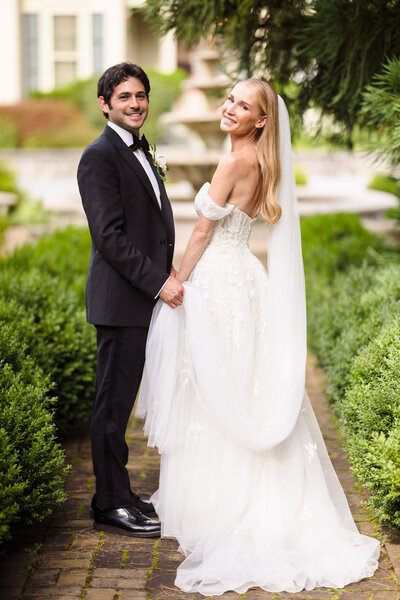 Romantic rooftop proposal in New York City with Elegant bride and groom holding hands in a lush garden path, smiling just after their wedding ceremony. view of One World Trade Center, as the groom kneels surrounded by rose petals and candles, captured by NYC wedding photographer Heritage House.