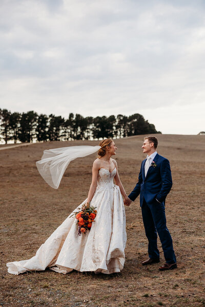 Romantic moment between bride and groom holding hands during their wedding sunset portraits session atop the hill at Petrichor Farm, Gundaroo NSW. By Acacia & Grace Photography