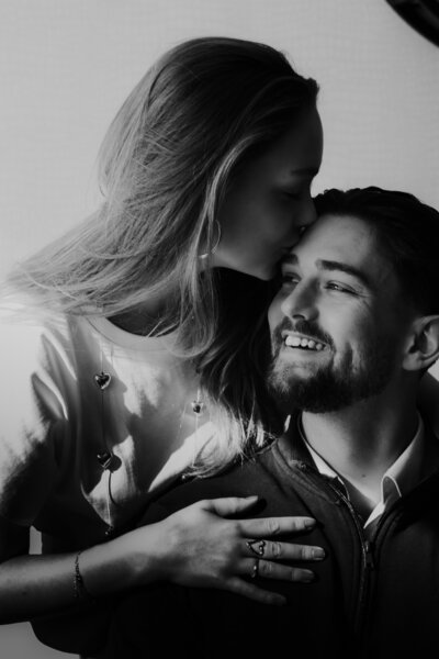 Een man en vrouw delen een kus voor een klok, een intiem moment in een tijdloos decor.