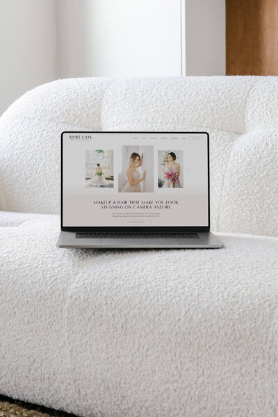 A wedding hair and makeup artist website is up on an open laptop sitting on a fluffy white couch.