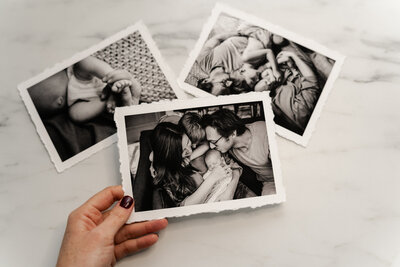 A hand holding a black and white photo of a family huddled together, with parents gently embracing their newborn.