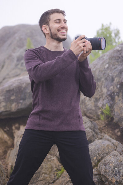 Guy holding camera in black t shirt standing in front of mountains