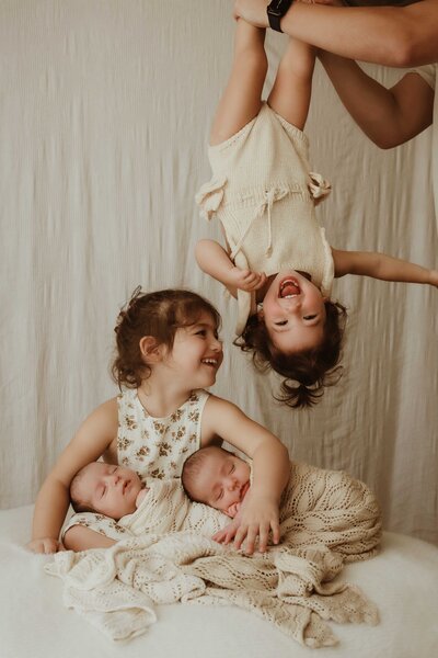 Sibling holding newborns while sibling is being held upside down, captured by Sydney newborn photographer Sophie Lea.